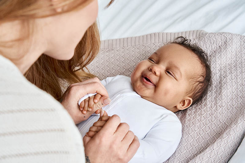 Caucasian mum holding hands of happy cute infant african baby girl daughter.
